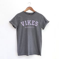 Support your team in style with our Minnesota Vikings Unisex T-Shirt, crafted from 100% ring-spun cotton for ultimate comfort and durability. Whether you're cheering from the stands or watching from home, this shirt is perfect for showing off your Vikings pride. The soft, breathable fabric ensures a great fit for every fan, making it an essential addition to your game day wardrobe.  Get your Minnesota Vikings t-shirt today and join the Skol nation in true comfort and style! SKOL VIKES! Product D Cotton Slogan T-shirt For Fan Gear, Gray Cotton T-shirt With School Spirit, Cotton Team Spirit T-shirt With Slogan, Team Spirit Relaxed Fit Pre-shrunk Shirt, Gray Team Spirit Cotton Top, Gray Cotton Team Spirit Top, Gray Cotton School Spirit T-shirt, Graphic Tee T-shirt With Team Name In Cotton, Graphic Tee With Team Name In Cotton