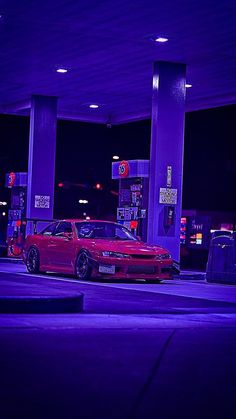 a red car parked in front of a gas station at night with purple lights on