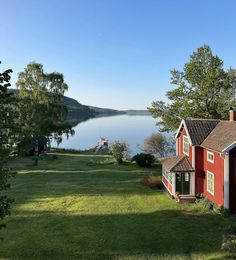 a red house sitting on top of a lush green field next to a body of water