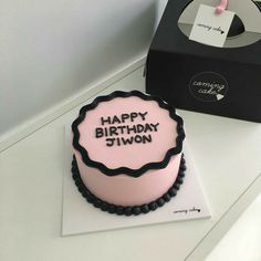 a pink and black birthday cake sitting on top of a table next to a box