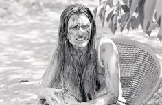 black and white photograph of a woman covered in mud sitting on a bench with her face smeared