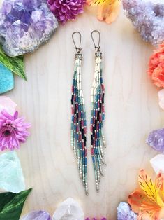 two pairs of beaded earrings sitting on top of purple and pink flowers next to each other