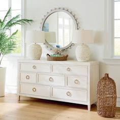 a white dresser with two lamps and a round mirror