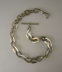 This is a low grade silver chain. What does that mean? Most silver chains we sell are English silver with clear hallmarks on every link. We also sell fancier chains which may be stamped Sterling. This chain has no silver marks. So we test it with acid for its purity and in this case get a low testing. So the silver content in the chain did not have enough to earn some sort of stamp. The chain is still an antique silver chain but the low grade purity is represented in the price. This is a massive chain which weighs 114g and measures 430mm in length. The chain is made up of a single length of large curb links with the largest being 19mm by 14mm. The chain also has an oversized dog clip and T bar - I have taken comparison shots of a regular sized dog clip and T bar to give you an idea of size Silver Hallmarked Oval Link Chain Necklace, Silver Oval Link Chain Necklace Hallmarked, Antique Silver Link Necklace, Vintage Silver Curb Chain Jewelry, Vintage Sterling Silver Chain Necklace With Lobster Clasp, Vintage Silver Jewelry With Curb Chain, Classic Silver Necklace With Hook And Links, Silver Engraved Chain Necklace For Formal Occasions, Silver Oval Chain Necklace For Formal Occasions