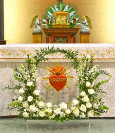 an altar with white flowers and greenery in front of a heart - shaped decoration