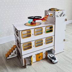 a toy car is parked in front of a cardboard dollhouse with cars on the floor