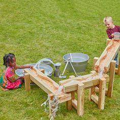 two children are playing in the grass with buckets and wooden structures on it,