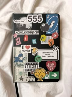 a notebook covered in stickers on top of a white sheet with a black cord