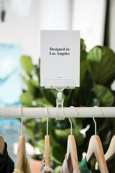 there is a sign that says designed in los angeles on clothes hangers next to a potted plant