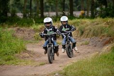 two young boys riding dirt bikes on a trail in the woods with grass and trees behind them