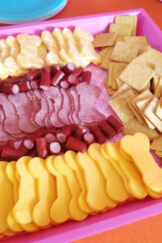 a platter with meat, cheese and crackers on it next to other foods