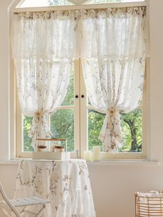 a white table and chair sitting in front of a window with curtains on the windowsill