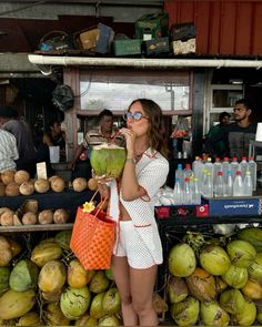 a woman standing in front of a display of coconuts and drinking from a straw