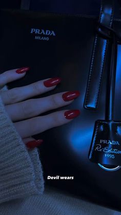 a woman's hand with red nail polish next to a black bag and blue light