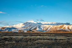 the mountains are covered with snow and brown grass in front of it is a blue sky