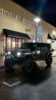 a black jeep parked in front of a store at night with its lights turned on