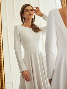 a woman in a white dress looking at her reflection in the mirror while wearing earrings