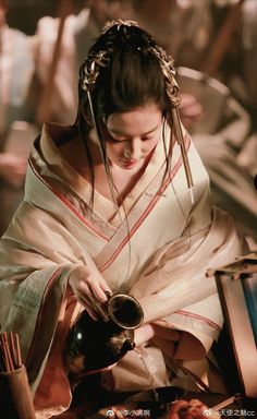 a woman dressed in traditional japanese garb pouring tea into a cup, with other items around her