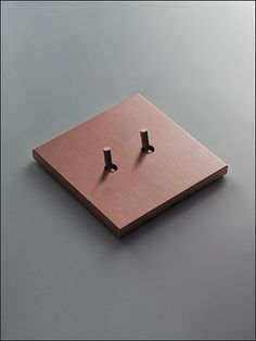 a square metal object with two small black crosses on it's side, sitting on top of a gray surface