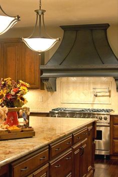 a kitchen with wooden cabinets and marble counter tops, an oven hood over the stove