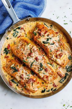 two pieces of fish covered in cheese and spinach on top of a skillet