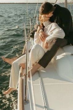 a man and woman sitting on the back of a sailboat kissing each other in front of an ocean