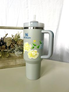 a travel mug with yellow flowers painted on it sitting next to a window sill