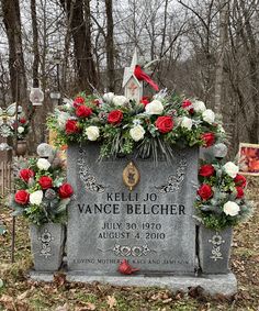 a headstone with flowers and greenery on it in the middle of a cemetery