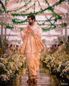 a man is walking down the runway in a white outfit with flowers around his neck