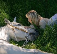 a woman laying in the grass next to a white horse