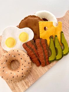 an assortment of felt food items on a wooden board, including eggs, bacon, and bread