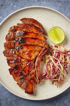 a plate with meat, cole slaw and lime wedges on it next to a slice of lime