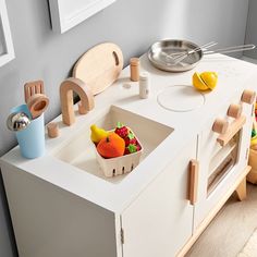 a toy kitchen with wooden toys on the counter and in front of it is a bowl of fruit