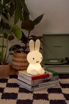 a rabbit lamp sitting on top of books next to a potted plant and television