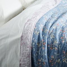 an unmade bed with white sheets and blue floral bedspread on top of it