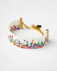 a white beaded bracelet with gold clasps and colorful beads on the end, sitting on a white surface