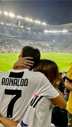 two people hugging each other in front of a crowd at a soccer game with the stadium lights on