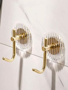 two clear glass holders with gold handles on a white wall next to a pair of brass - plated hooks