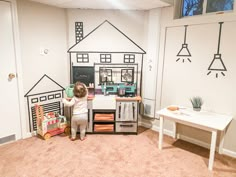 a young child playing with toys in a playroom that is white and has black drawings on the walls