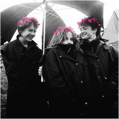 black and white photograph of three people standing under an umbrella with pink flowers in their hair