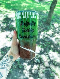 a person holding up a green cup with writing on it in the grass and trees