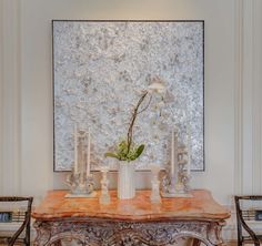 a table with candles and flowers on it in front of a large art piece,