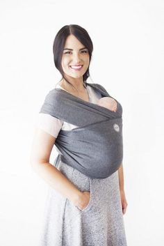 a woman wearing a grey wrap around her baby's back and smiling at the camera