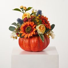 an orange pumpkin filled with flowers on top of a white table