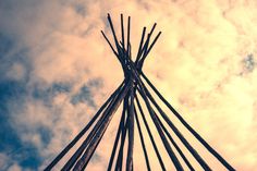 a tall metal structure with many sticks sticking out of it's sides against a cloudy blue sky