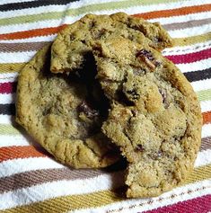 a chocolate chip cookie is cut in half on a striped cloth with a bite taken out