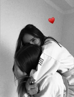 two girls hugging each other with a red heart in the air above them on a white wall