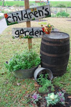 a wooden barrel sitting in the grass next to a sign that says children's garden