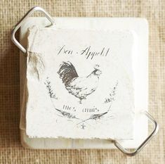 a square stone coaster with a rooster on it and the words fau appeti written in cursive writing