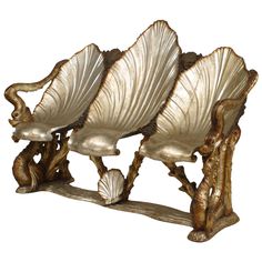 three golden chairs sitting next to each other on top of a white surface with gold leaves